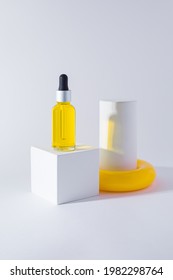 White design cubic podium with small bottle of essential oil on it. White cylinder with yellow ring around, placed near. Mockup design for cosmetics. Copy space, white background - Shutterstock ID 1982298764