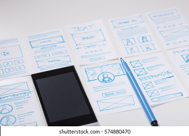 White designer desk with smartphone and mobile app screen drawings. Developing mobile responsive websites