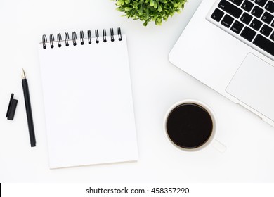 White Designer Office Desk Table With Blank Notebook Page With Pen, Laptop Computer And Cup Of Coffee. Top View, Flat Lay.