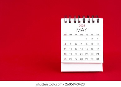 White desk calendar for May 2025 on red color background.