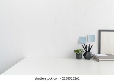 White desk, with empty space. Workspace with design supplies, flowers in a vase against white wall. 