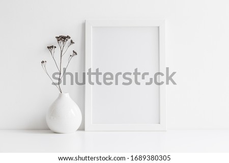 White desk with photo frame and  minimal round vase with a decorative twig against white wall. 