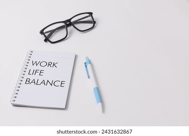 A white desk setup showcasing a notebook with Work Life Balance written on it, blue pen, black glasses symbolizing job opportunity and office work environment