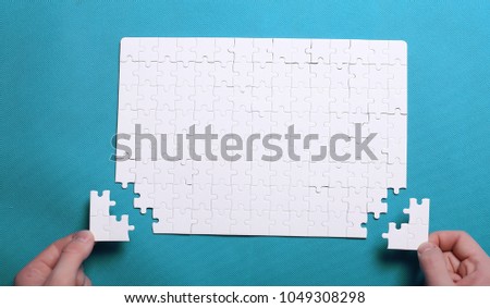 White details of puzzle on background. A puzzle is a puzzle from small pieces. Heart shape of the details. Hands folding puzzle in white.