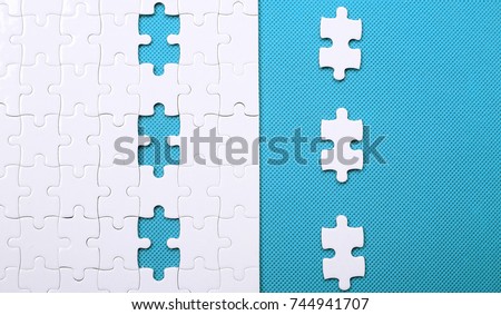White details of puzzle on background. A puzzle is a puzzle from small pieces. Heart shape of the details. Hands folding puzzle in white.