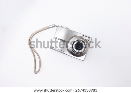 white digital compact camera seen from the front against a white background, photographed from a top angle