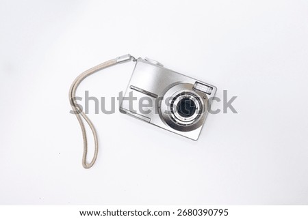 white digital compact camera seen from the front against a white background, photographed from a top angle