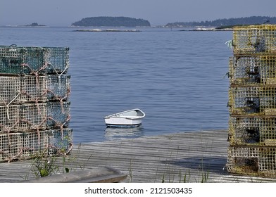 White dinghy, distant offshore islands, and lobster traps stacked on wooden dock in South Thomaston, Maine.