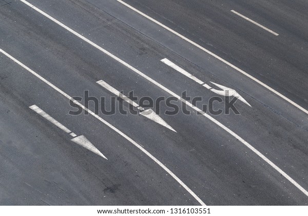 White\
directional arrows on asphalt road - top\
view.