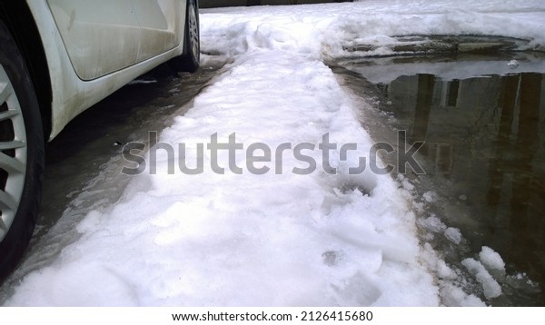 White Dirty Car parking on snow road with puddle.\
Messy, salt, chemicals in early spring. Tire. Ecology problem in\
city. Protection and wash vehicle concept. Driving. Auto.\
Snowstorm. Snow melts.