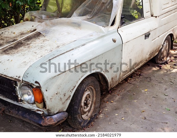 White dirty old\
auto with flat tires. Dirty white old model car with flat tires\
stands covered with\
polyethylene