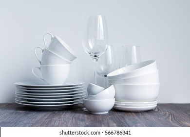 White dishware stacked on a wooden table against white background with transparent wineglasses