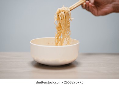 white disposable plastic fork with cooked instant noodles over blurred disposable paper cup with aluminum foil lid on wooden background. Eating behavior, effects of instant noodles on human health.