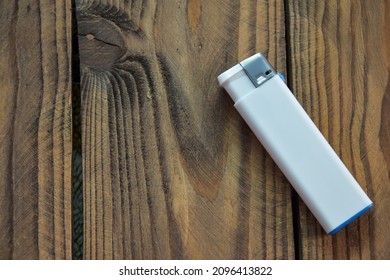 A white disposable plastic lighter is positioned on a wooden background. Top view of a white lighter and a place to place the text. Blank mock up cigarette lighter. Cigarette lighter template.