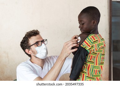 White Doctor With Face Mask And Glasses, Putting A Cotton Ball On The Injection Site On The Arm Of A Small African Patient After Vaccination