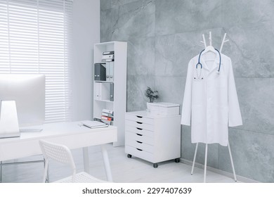 White doctor's gown and stethoscope hanging on rack in clinic