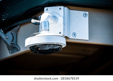 A white dome security camera with a reflective lens is attached to a building's exterior wall, showing a discreet surveillance system