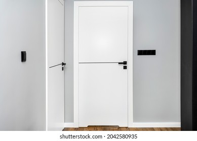 A white door with a ventilation undercut with a matte black handle and a black line in the middle in a modern house with vinyl panels on the floor.