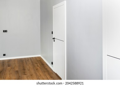 A white door with a ventilation undercut with a matte black handle and a black line in the middle in a modern house with vinyl panels on the floor.