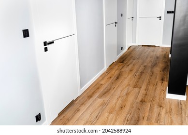 A white door with a ventilation undercut with a matte black handle and a black line in the middle in a modern house with vinyl panels on the floor.