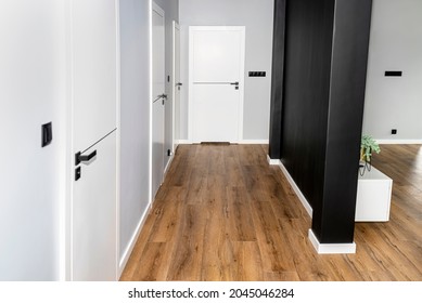 A white door with a ventilation undercut with a matte black handle and a black line in the middle in a modern house with vinyl panels on the floor.