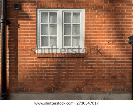 White double-hung windows fixed into the ground floor of a plain Georgian red brick building. Black drain spouts on either side. Strong shadows on a sunny winter morning. 