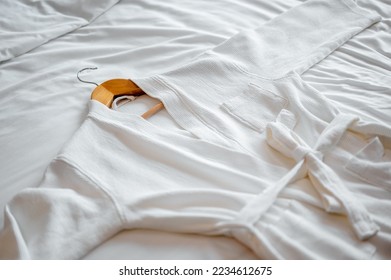 A white down bathrobe decorated,soft and comfortable fabric, hung on hanger on a bed with white linens.It is a set for hotel guests to use while bathing or wear bathing suit.Time to travel, journey,