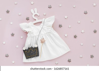 White Dress With Kids Handbag Shape Of Crown On Cute Hanger With Bunny Ears. Set Of  Baby Clothes And Accessories For Spring Or Summer On Pink Background. Fashion Childs Outfit. Flat Lay, Top View