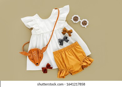 White Dress,  Orange Shorts With Kids Handbag And Sunglasses. Set Of  Baby Clothes And Accessories For Spring Or Summer On Beige Background. Fashion Childs Outfit. Flat Lay, Top View