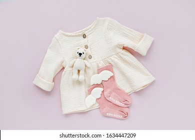 White Dress With Pink Socks And Toy Bear. Set Of Baby Clothes And Accessories For Spring  Or Summer On Pastel Background. Baby Shower Concept.  Fashion Kids Outfit. Flat Lay, Top View