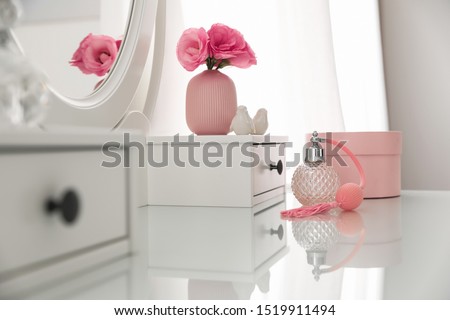 White dressing table with decor and bottle of perfume in room
