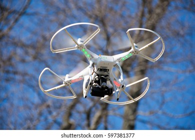 white drone with camera hovering in trees