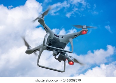 White drone quadcopter taking off from the ground on background of blue sky.