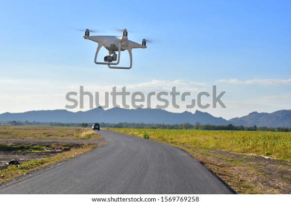 White drone take off from land and flying for take\
aerial photo. at sunset evening blue sky and above curve road front\
of hill.