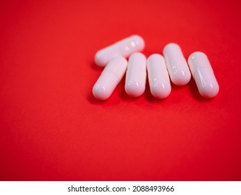 White drug capsules on colored red paper texture background. Macro close up pill medication. Big pharma. Off label approved medicine drugs use. Pharmacy concept. Copy space. Mock up design template.