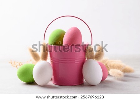 White easter eggs with bunny rabbit ears and colorful easter eggs in pink bucket on white background