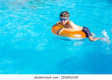 White Eastern European Boy 9 Years Old Wearing Goggles On A Swim Ring In The Pool. Side View