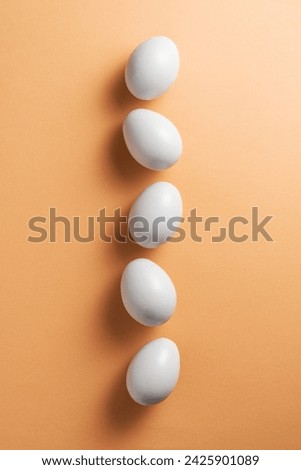 White eggs aligned in a row on orange background, directly above, high angle shot