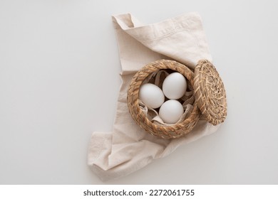 White eggs in brown basket with lid on white cloth