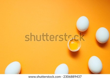 White eggs and egg yolk on the yellow background. Egg yolk in egg shell, cracked egg white isolated on orange background