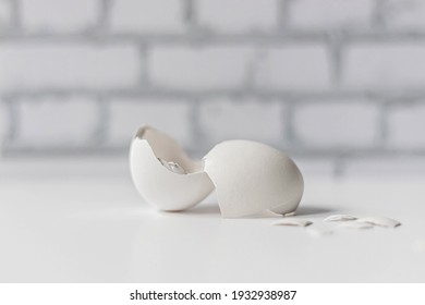 White Eggshell Of A Broken Chicken Egg With Shards Isolated On A White Background. White Brick Wall In The Background. Easter.