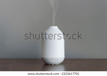 White electric aroma diffuser on a pedestal table. Indoor air freshener and humidifier with steam. Cleaning device for fresh air and healthy life