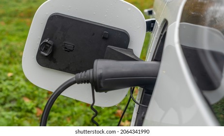 White Electric Car Is Charged In The Village. Outside The City The Countryside. Private Electric Car Charger. Electric Charge In A Village House