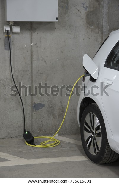 White Electric car charging in a house garage\
with power plug inserted