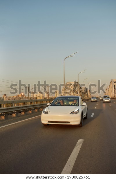 White\
electric car with driver and passenger moving along aspalted city\
road, vertical shot. Luxury and success\
concept