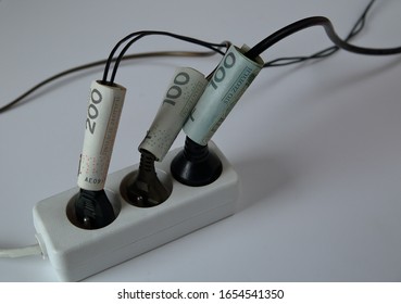 White electric extension cord with three black plugs clsoe up on white background, wires tied with banknotes of 200 and 100 Polish zloty, concept of high costs of electricty