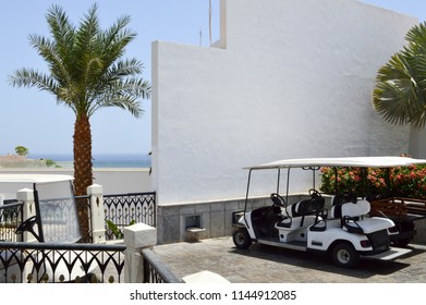 White electric golf cars are parked in small electric vehicles with awnings from the sun in a warm tropical southern exotic holiday resort country.