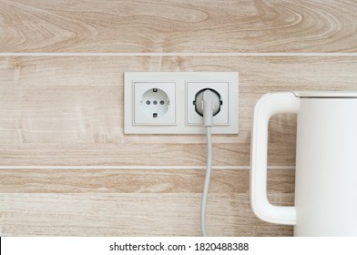 White Electric Kettle Plugged Into A Power Outlet On A Wall Into A Kitchen