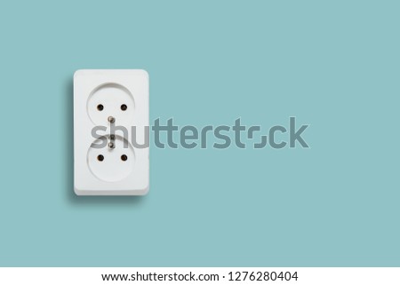 White electric socket on blue pastel background. The concept of electric power consumption, use of electricity. Savings on energy supply, power supply of various household items. Minimalist photo.