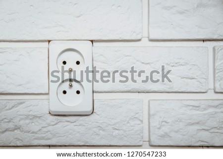 White electric socket on a white, bright brick. The concept of electric power consumption, the use of electricity. Savings on energy supply, power supply of various household items.